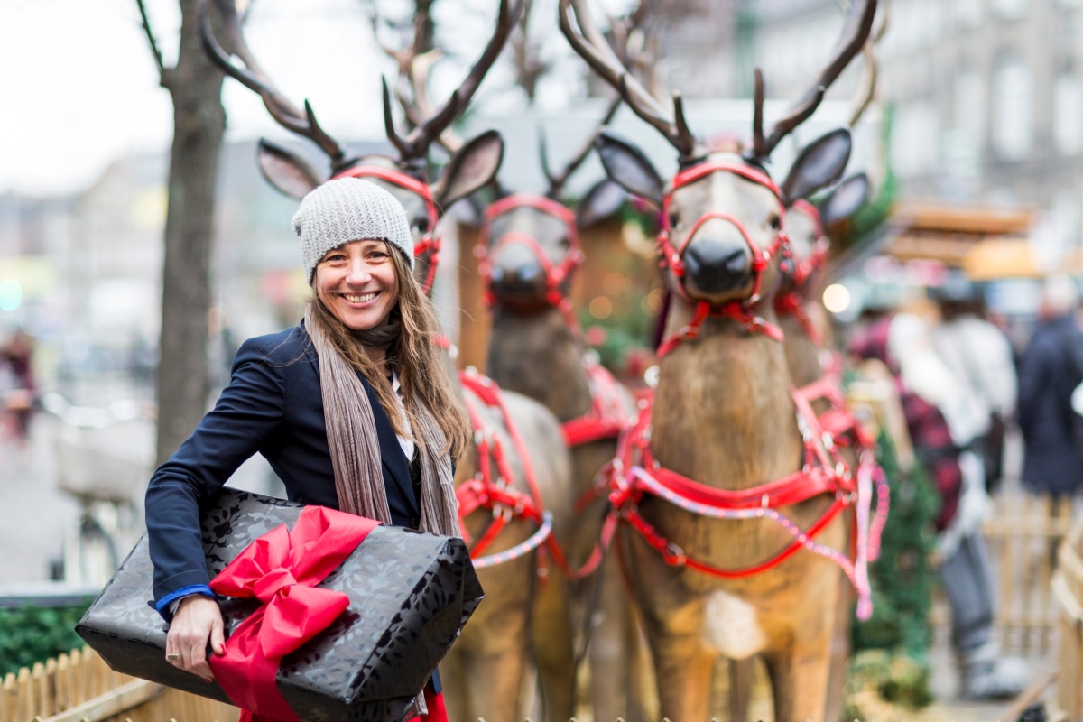 Portrait of mature woman with Christmas gift in front of reindeer display, Copenhagen, Denmark