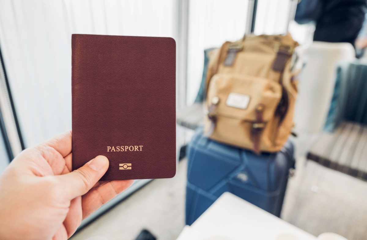 close up hand holding passport at airport terminal with suitcase and backpack at airport