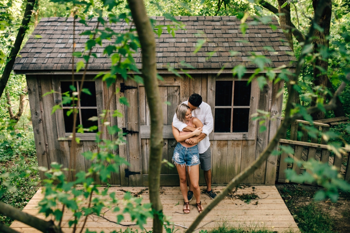 Couple embracing in front of a rustic cabin surrounded by lush greenery