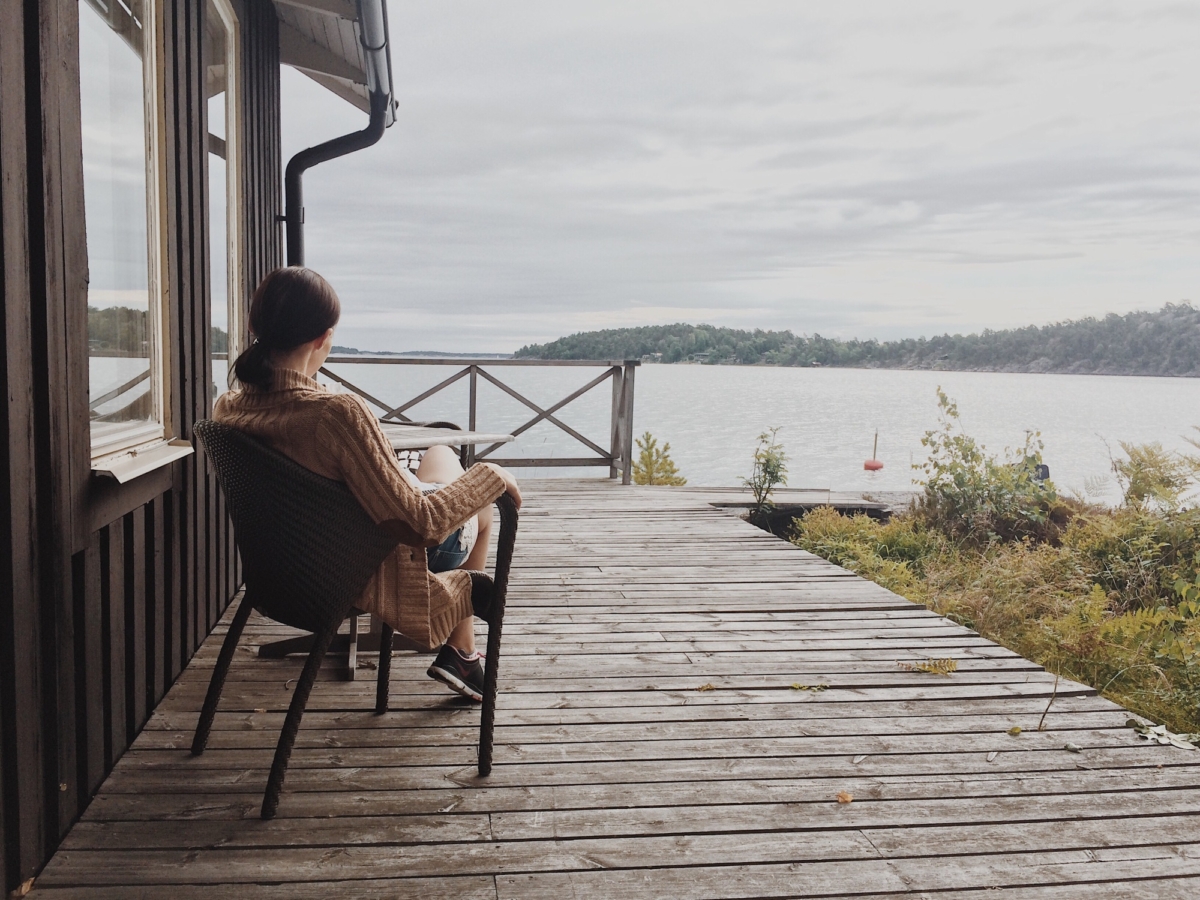 Young woman sitting on a terrace of a cabin overlooking a lake